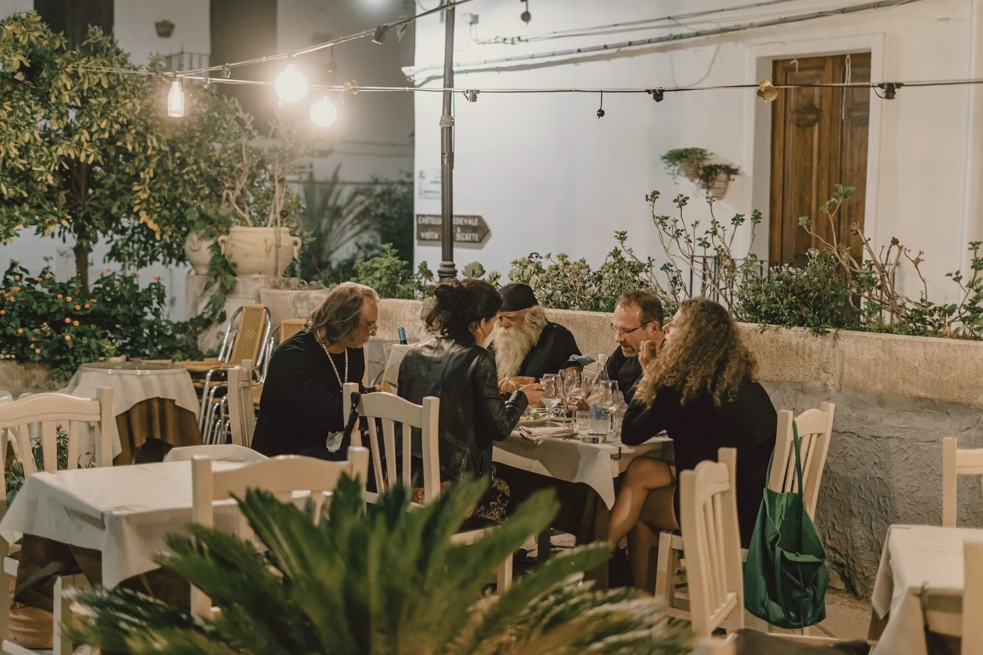 People still at the table after dark under festoon lights, between whitewashed walls and potted lemons.